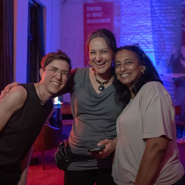 Three people pose side-by-side facing the camera, their arms around each other. They are all smiling brightly.