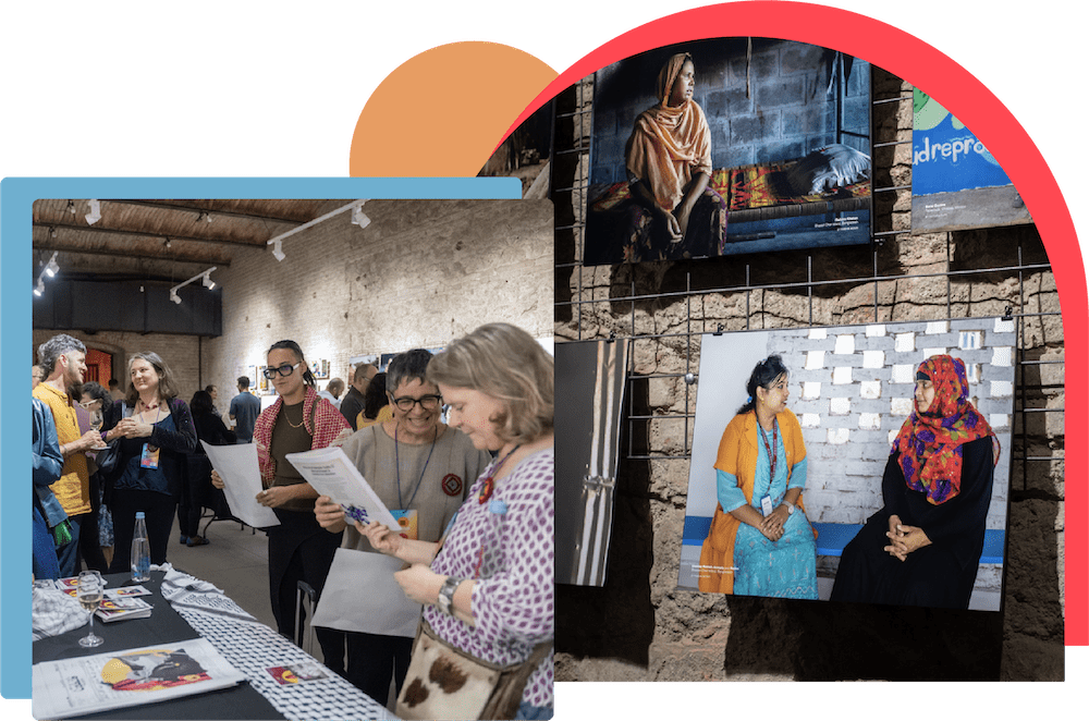 Image on Right Side: A photo of a printed photo that is hung on a wire grid. The printed photo features two women sitting together facing each other. One is wearing a bright blue dress and orange scarf, her long dark hair tied back. The other is wearing a colorful red and purple head scarf over a black dress. Image on Left Side: Several people stand in pairs and small groups in a large and bright indoor space. In the foreground to the right, two people are standing beside a table looking together at a flier. A third person is approaching the table holding a flier. Two people in the background are facing each other and appear to be in the middle of conversation.
